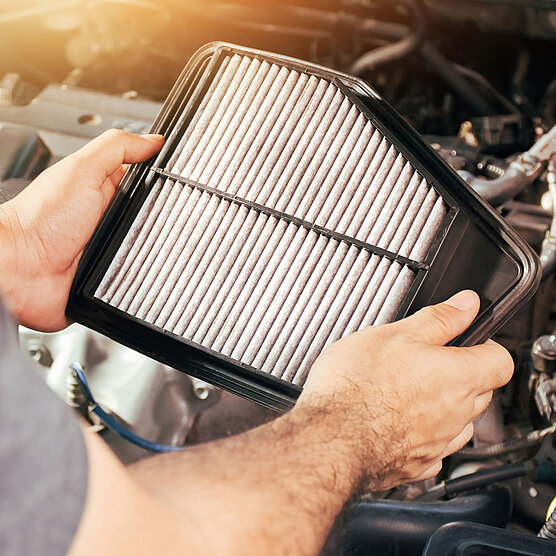 Hands inserting a paper air filter into the engine compartment