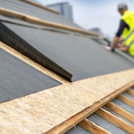 Worker placing nonwoven sheet over the wooden substructure of a house roof